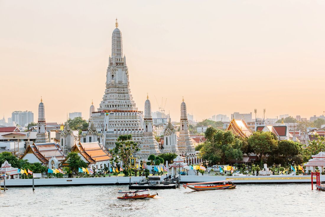 Wat Arun Temple in Bangkok with Cho Phraya river and Bangkok skyline at sunset