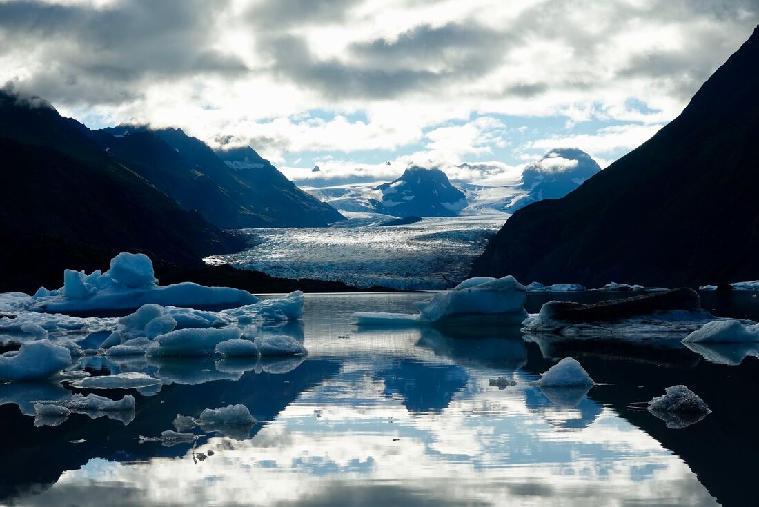 Grewink Glacier is nestled between two mountains with large ice floes in the foreground in a lake