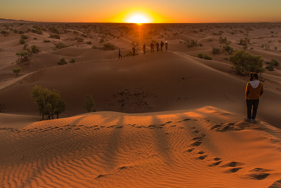 Group of travellers stand on a dune looking out at the sunset in Erg Chigaga 