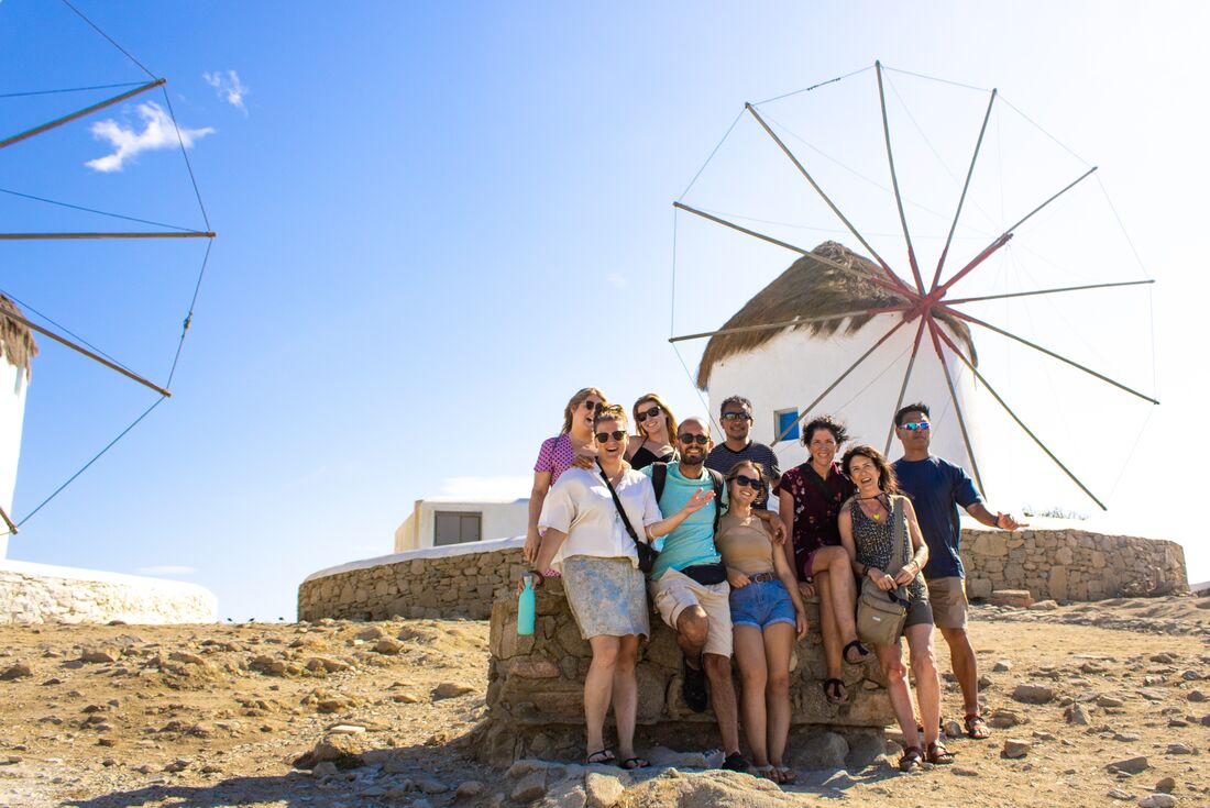 Travellers pose for a group shot with the iconic windmills of Mykonos in the Cyclades 