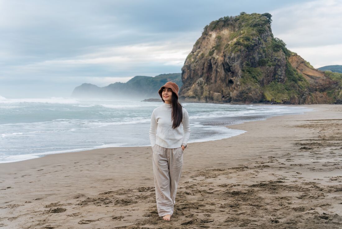 Traveller walking down Piha Beach with Lion Rock in the background in Auckland, New Zealand