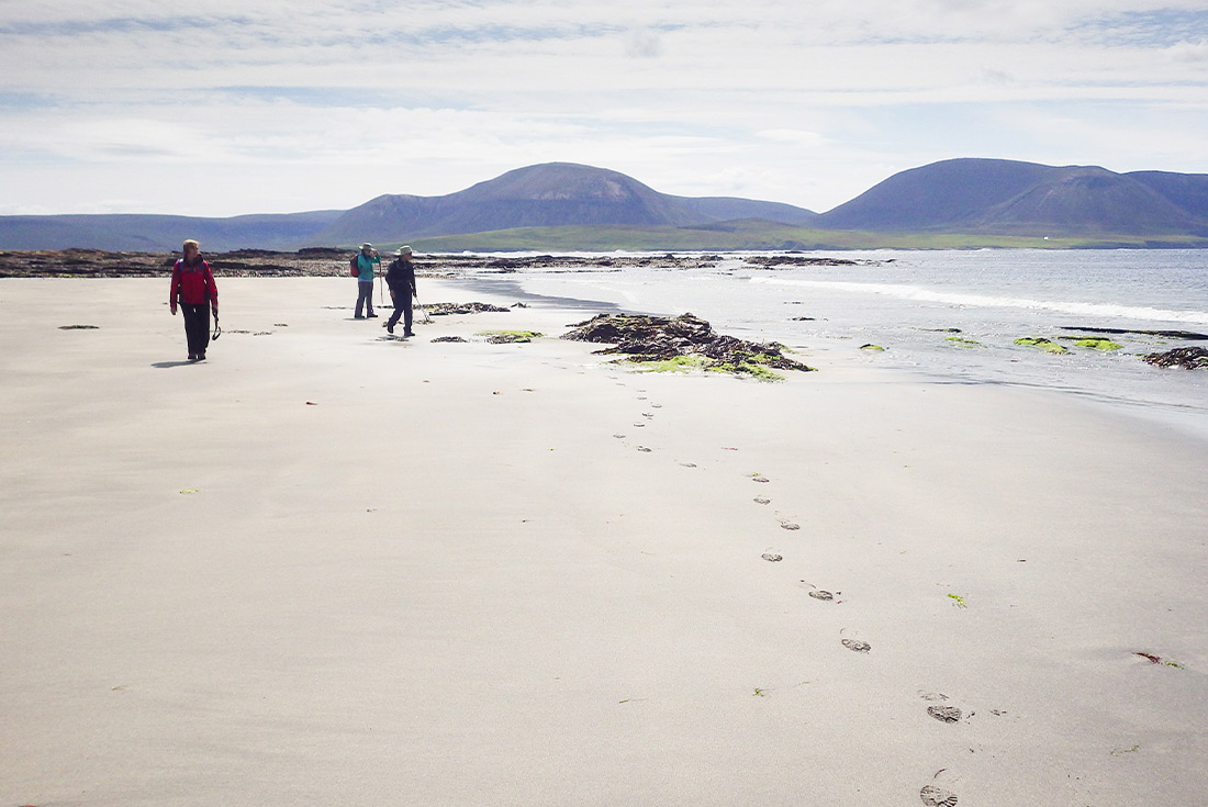 Travellers walking across Orkney Beach, United Kingdom