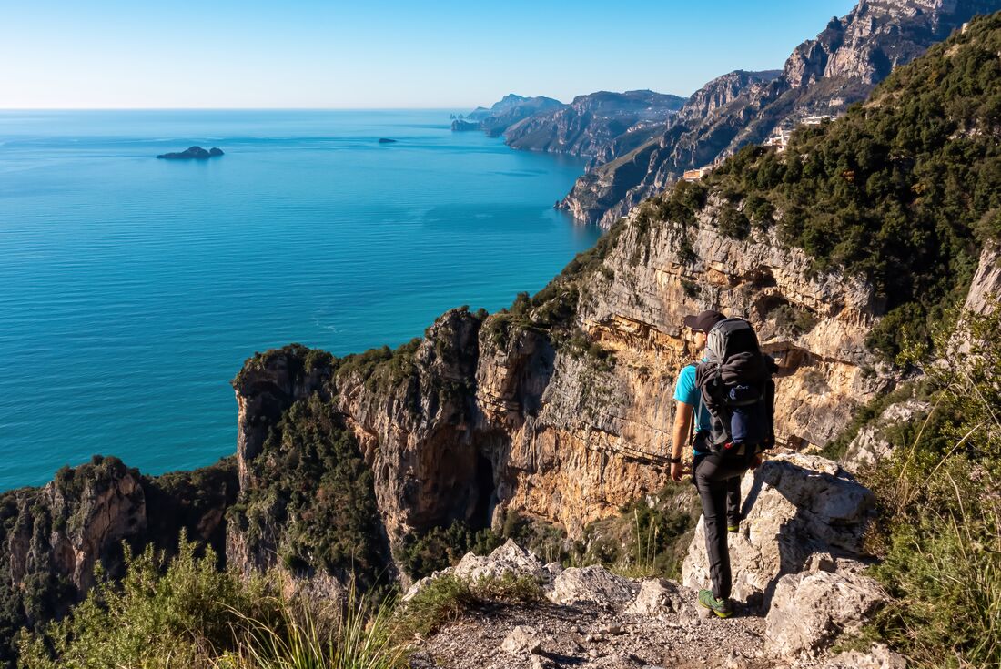 POV of traveller hiking high in the mountains in Praiano, Positano, Italy, looking out to the blue ocean and blue sky horizon