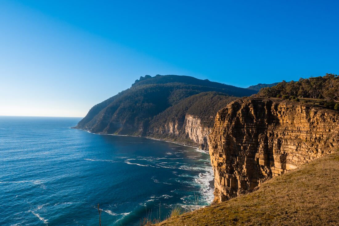 View from the coast look out on clear blue sky day, with blue waters and golden cliff edge, Maria Island, Australia
