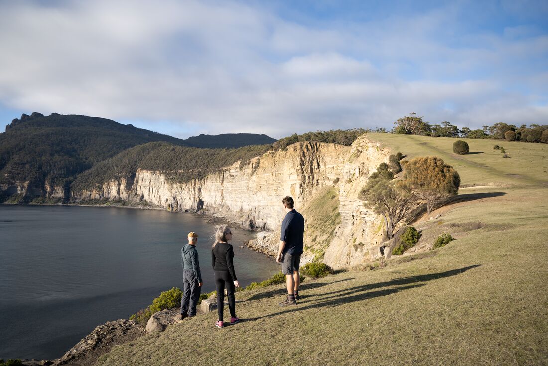 Travellers with guide looking out to the coast where the water meets the the cliffside on Maria Island, Australia