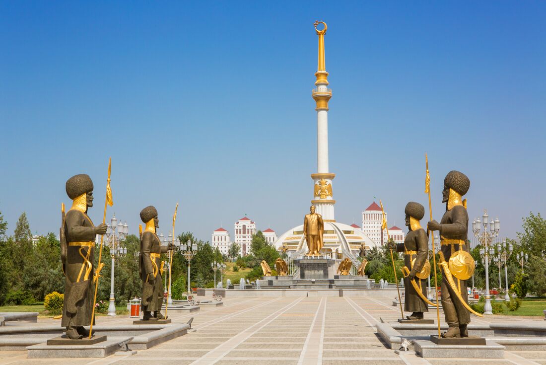 Turkmen statues flank Ashgabat Independence Monument in Turkmenistan with further statues and spires beyond