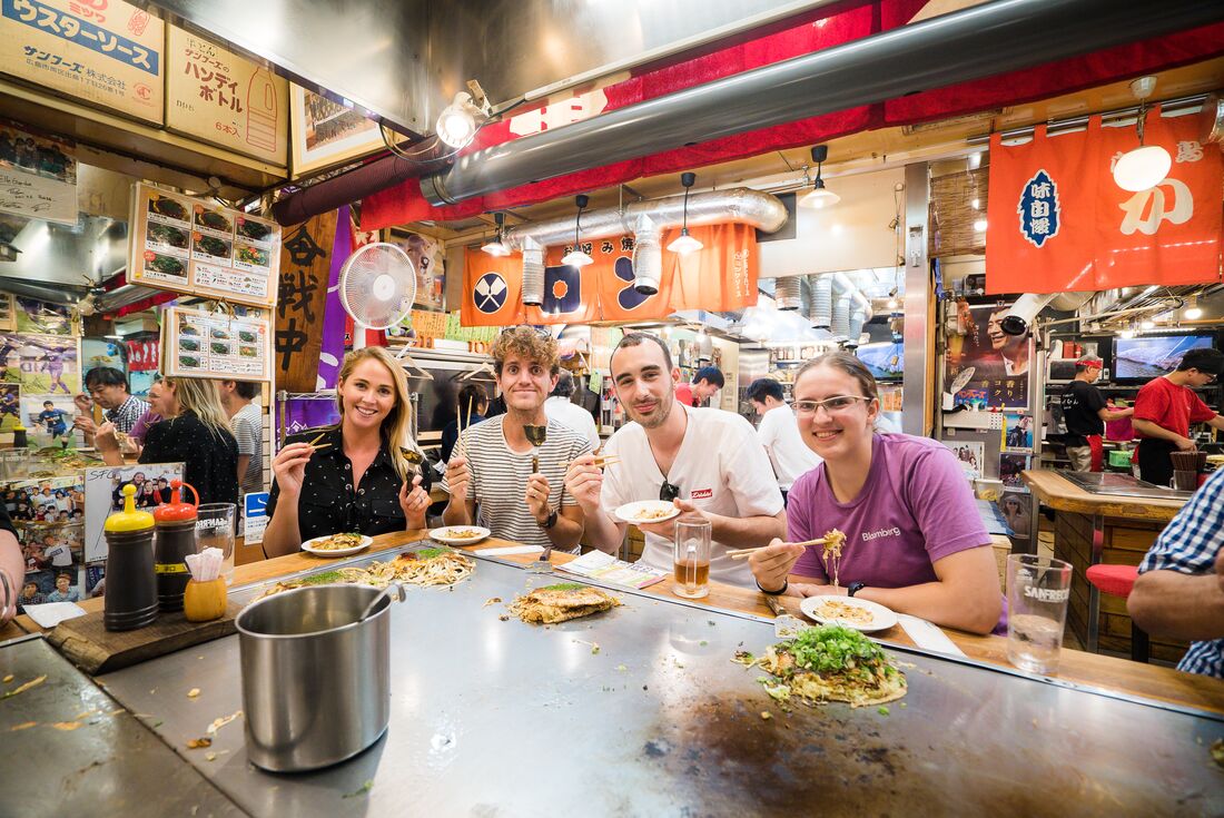 Travellers sit down to eat Okonomiyaki in Japan