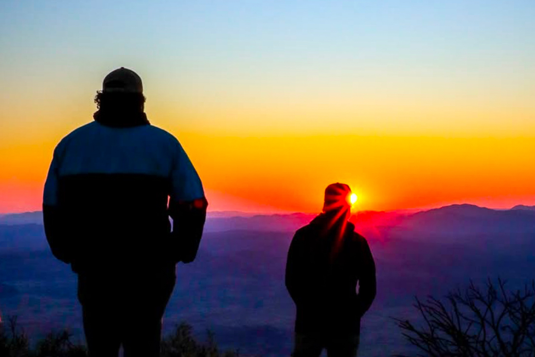 Intrepid leader Benji and traveller watch the sunset from the top of Mount Sonder