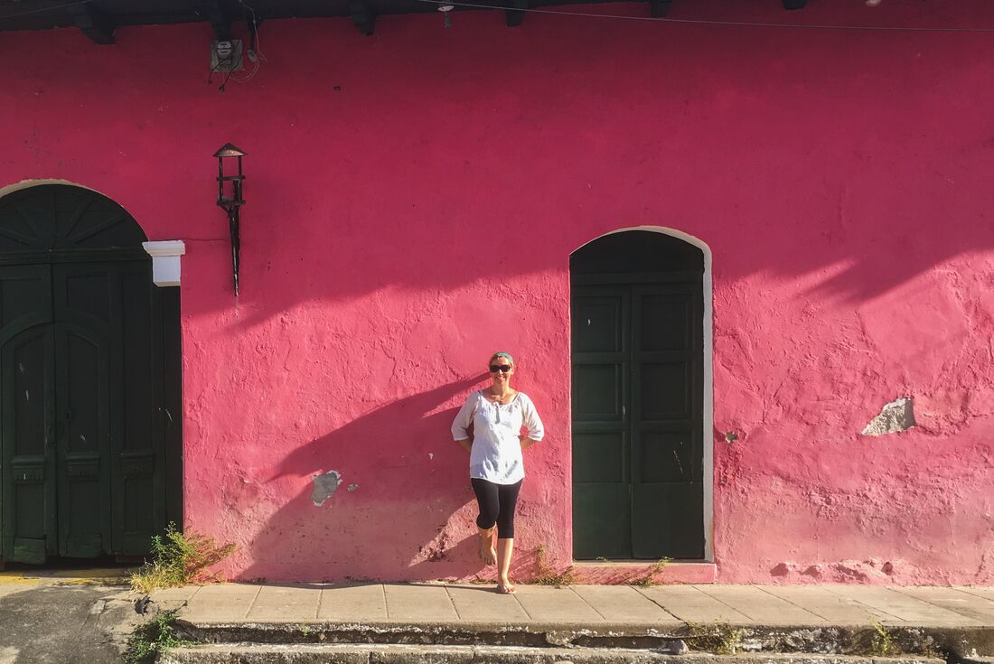 Traveller leans against a bright pink painted building in the streets of Suchitoto in El Salvador