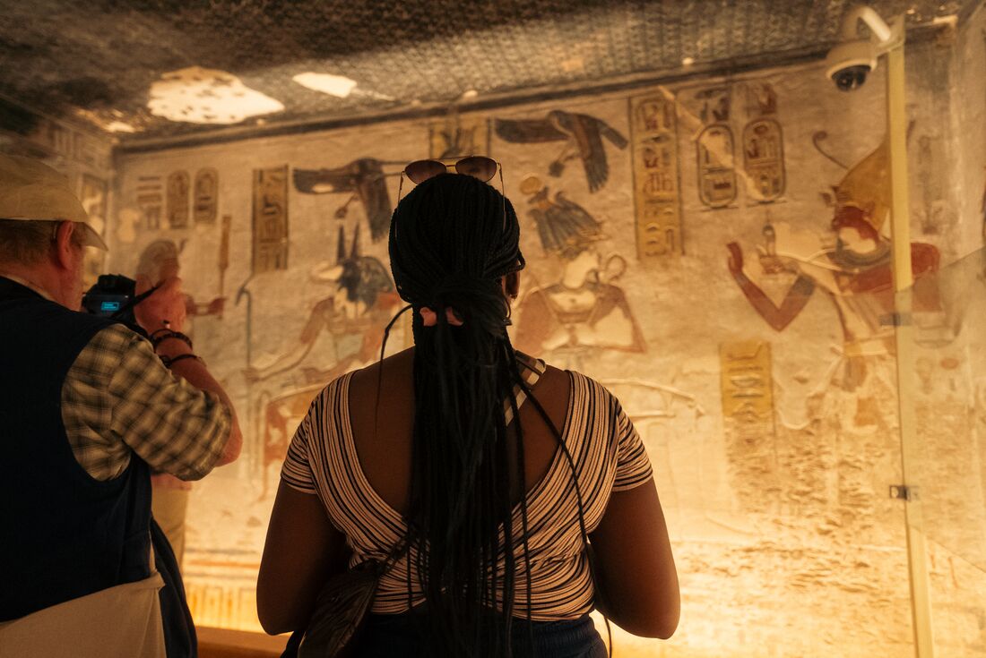 Traellers looking at hieroglyphic writing on wall at Valley of the Kings, Luxor, Egypt