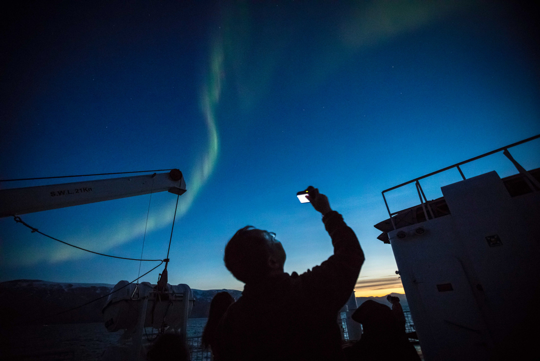 Traveller takes a photo up looking at the Aurora Borealis Northern Lights over east Greenland