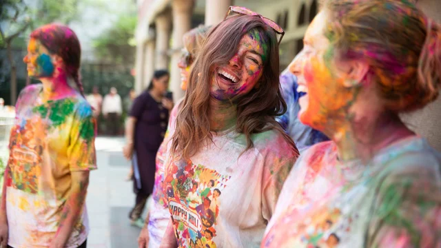 Two women smile at each other after taking part in Holi Festival celebrations in India.