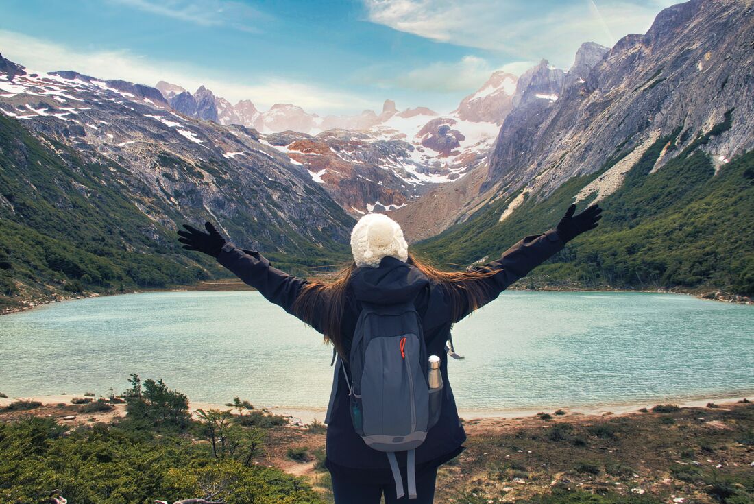 Traveller stands with outstretched hands overlooking green Laguuna Esmerelda with mountains in the background