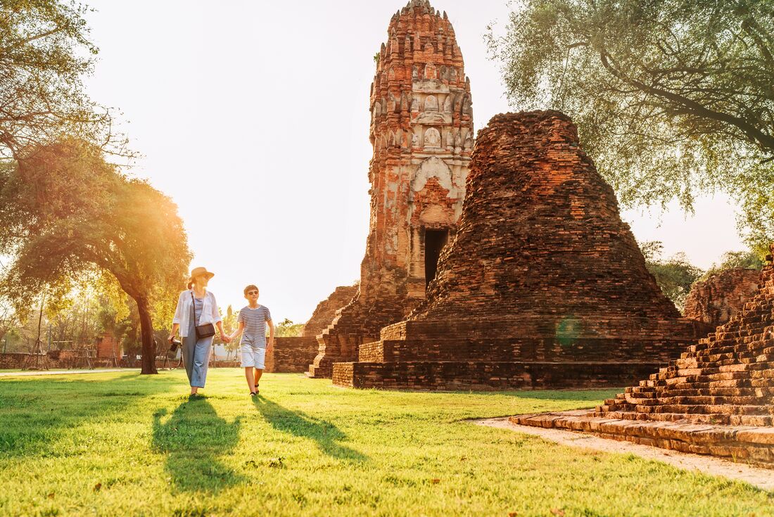 Mother and son walk through Wat Phra Mahathat temple in Atutthaya as sun shines through background