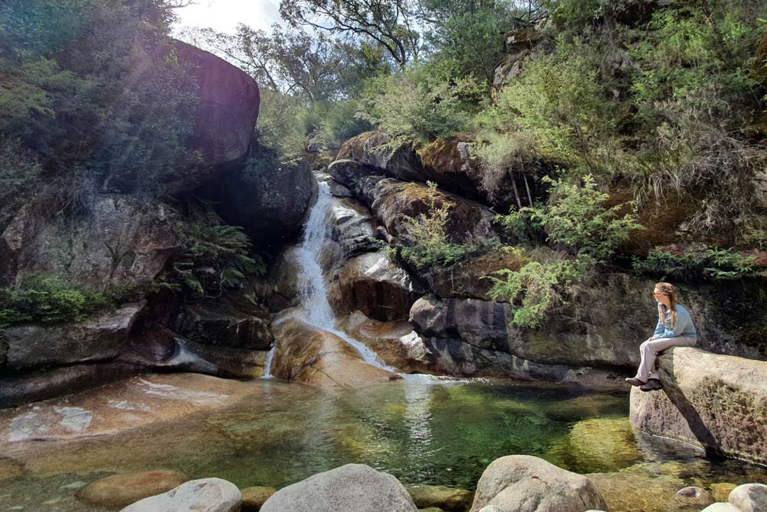 Woman sitting on rock in front of waterfall in Mt Buffalo National Park, Victoria High Country