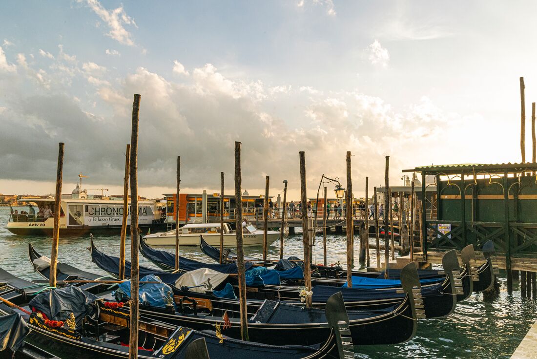 Gondolas docked along a peer during warm sunset light in Venice, Italy