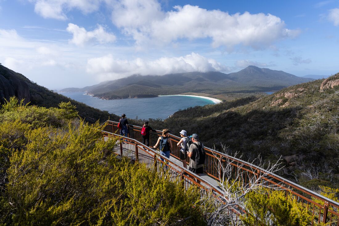 Group of Intrepid travellers look out over Wine Glass Bay from a lookout in Tasmania