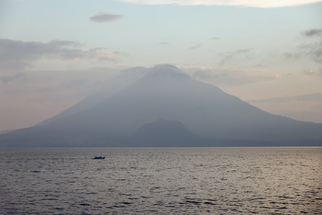 Calm Lake Atitlan with boat on the water and volcano in the background on a misty morning, Guatemala