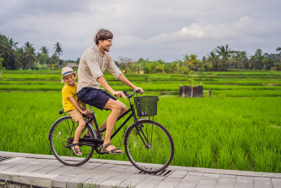A father and son happily cycling through rice fields in Ubud, a small town in the Bali province, Indonesia