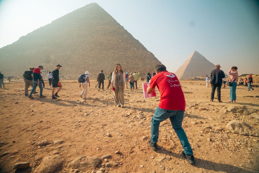Leader takes a photo of a traveller posing in front of the Pyramids of Giza, Egypt