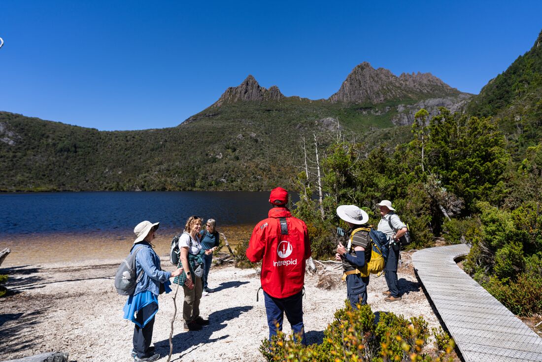 Travellers receive a talk from the leader on the shores of Dove Lake with Cradle Mountain looming behind