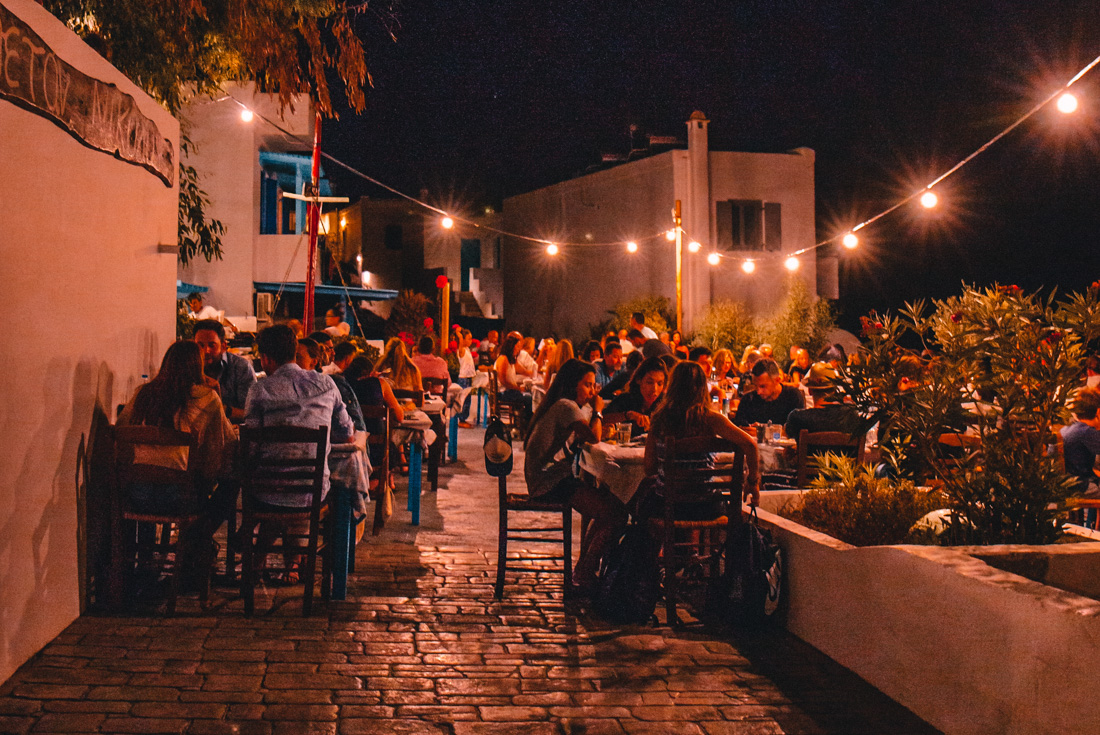 Travellers and locals all gathered at an outdoor seaside restaurant in the small Cyclades in Greece