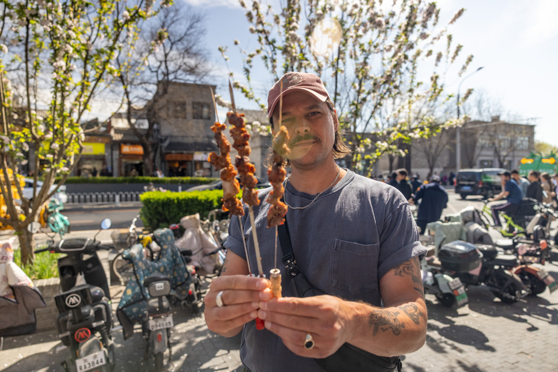 Intrepid traveller holds up Beijing lamb skewers, streetfood bought on a real food adventure tour in China