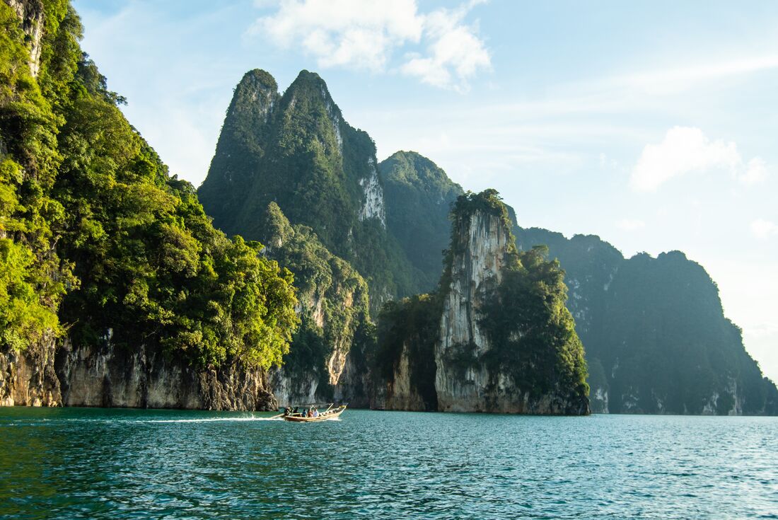 Longtail boat floats past huge limestone mountains in Khao Sok National Park in Thailand